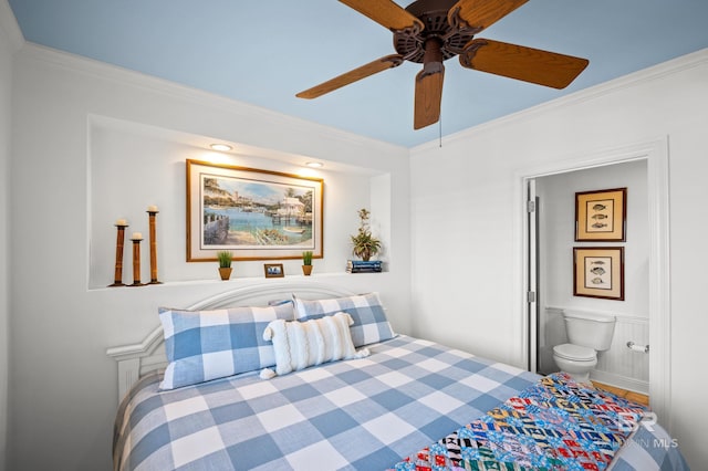 bedroom with ceiling fan, crown molding, a wainscoted wall, and ensuite bathroom