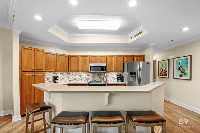 kitchen featuring light hardwood / wood-style flooring, stainless steel appliances, a raised ceiling, and crown molding