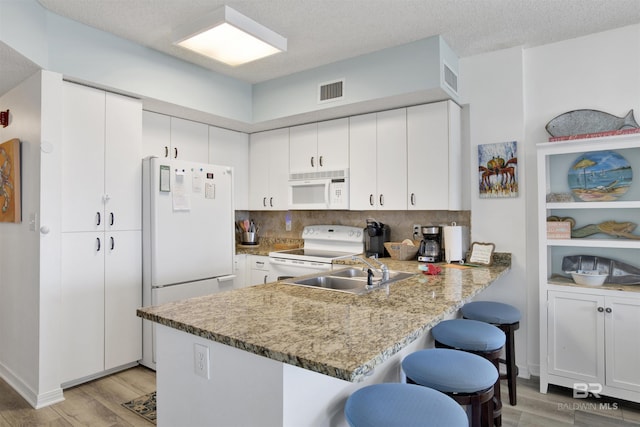 kitchen with sink, white cabinetry, kitchen peninsula, white appliances, and light hardwood / wood-style floors