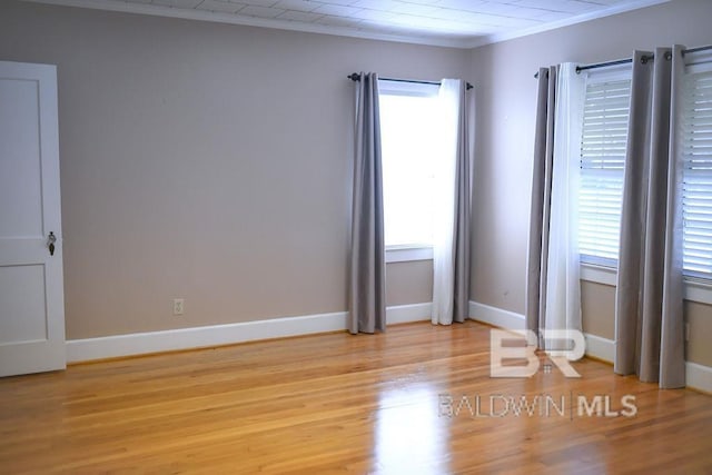 empty room with ornamental molding, light wood-type flooring, and a wealth of natural light