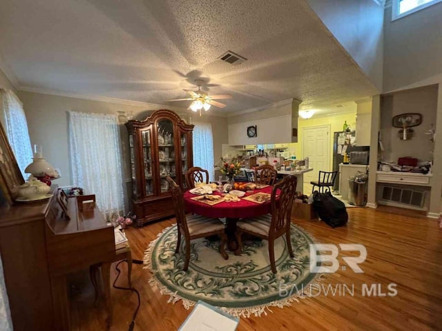 dining room with ceiling fan, wood-type flooring, ornamental molding, and a textured ceiling