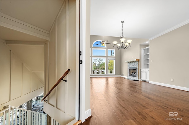 unfurnished living room featuring wood finished floors, baseboards, a fireplace with raised hearth, crown molding, and ceiling fan with notable chandelier