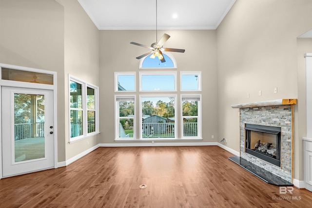 unfurnished living room with ornamental molding, wood finished floors, a fireplace, baseboards, and a towering ceiling