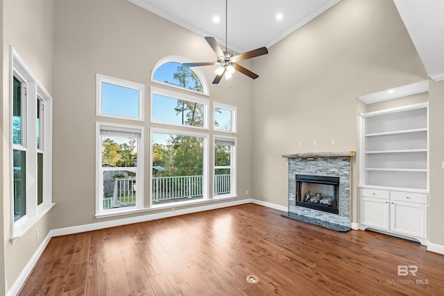 unfurnished living room with built in shelves, wood finished floors, baseboards, a ceiling fan, and a fireplace