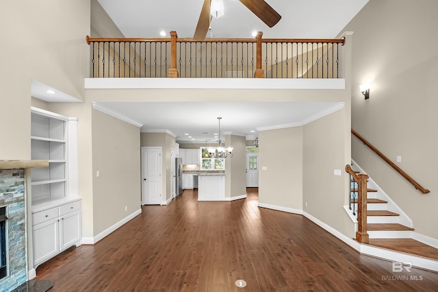 unfurnished living room with ceiling fan with notable chandelier, a fireplace, dark wood-type flooring, and baseboards