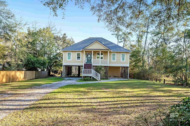 coastal home featuring driveway, covered porch, stairs, a front lawn, and metal roof