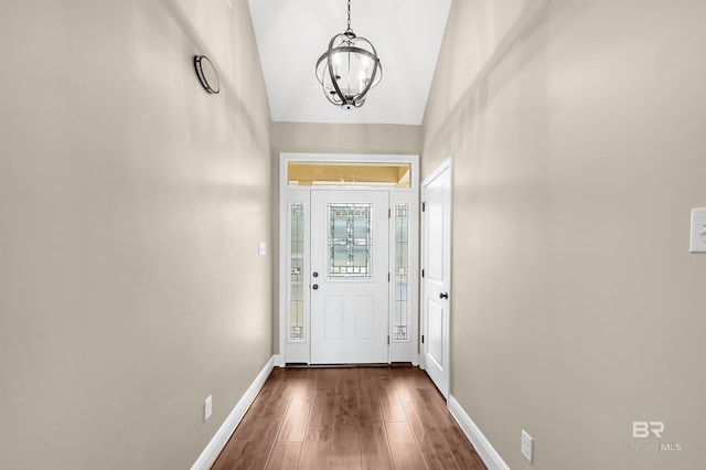 foyer featuring vaulted ceiling, dark wood-style floors, baseboards, and a chandelier