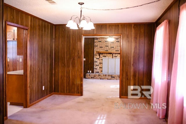 carpeted spare room featuring a textured ceiling, an inviting chandelier, crown molding, and wood walls