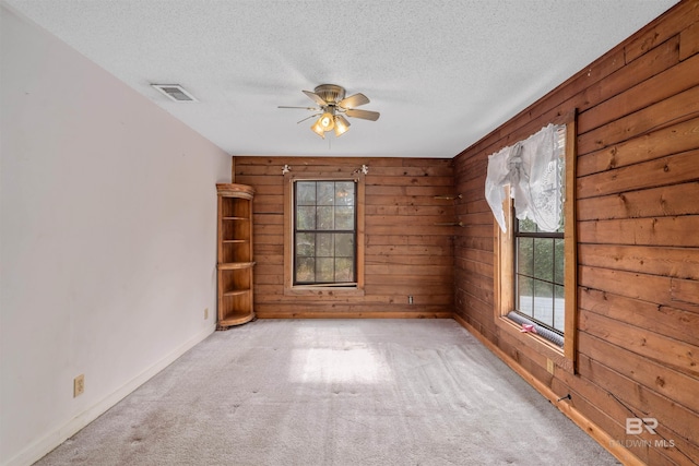 carpeted spare room featuring ceiling fan, wooden walls, and a textured ceiling