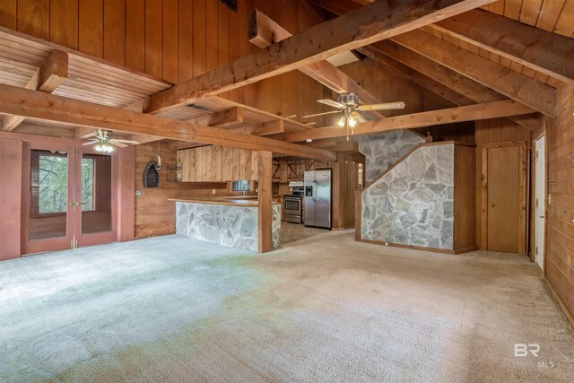 unfurnished living room with french doors, wood walls, lofted ceiling with beams, light colored carpet, and ceiling fan