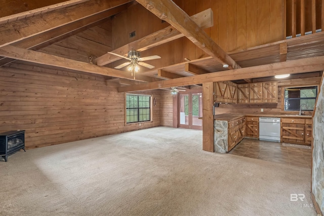 unfurnished living room with a wood stove, light colored carpet, and wooden walls