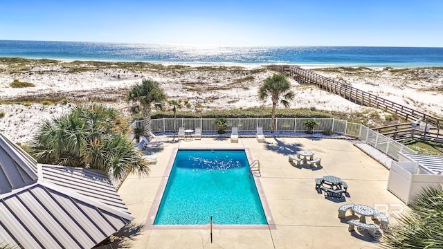 view of swimming pool featuring a patio, a water view, and a view of the beach