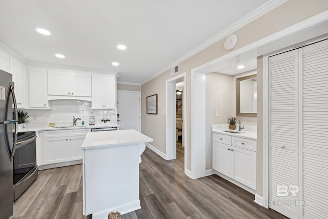 kitchen with sink, ornamental molding, appliances with stainless steel finishes, a kitchen island, and white cabinets
