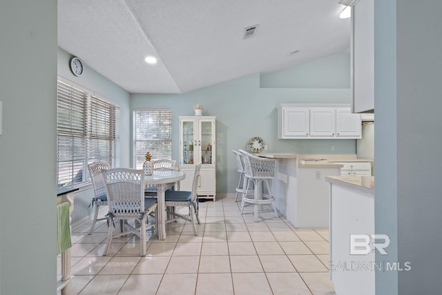 dining room featuring visible vents, baseboards, vaulted ceiling, light tile patterned floors, and a textured ceiling