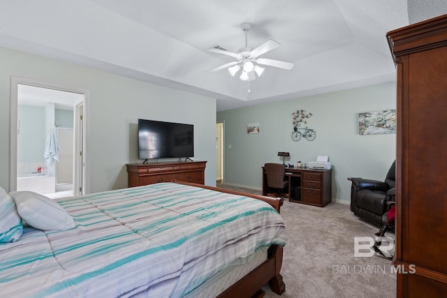 bedroom with a raised ceiling, ensuite bathroom, a ceiling fan, baseboards, and light colored carpet