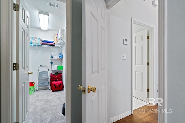 corridor featuring baseboards, visible vents, a textured ceiling, and carpet