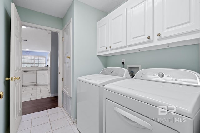 laundry room featuring washer and dryer, baseboards, cabinet space, and light tile patterned flooring