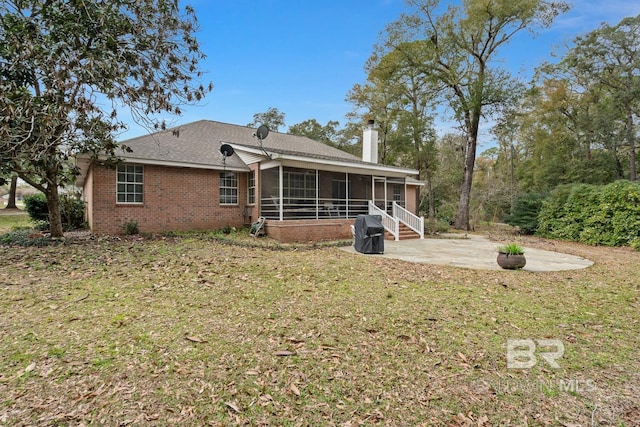 back of property with a sunroom, a chimney, a lawn, a patio area, and brick siding