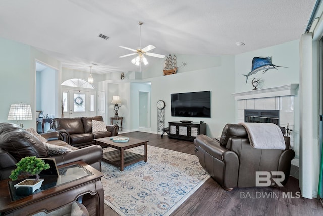 living room featuring visible vents, a tiled fireplace, dark wood-style floors, lofted ceiling, and ceiling fan