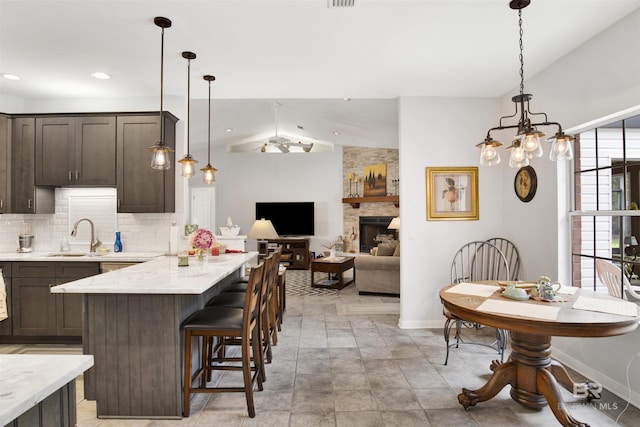 kitchen with lofted ceiling, a fireplace, a sink, dark brown cabinets, and tasteful backsplash