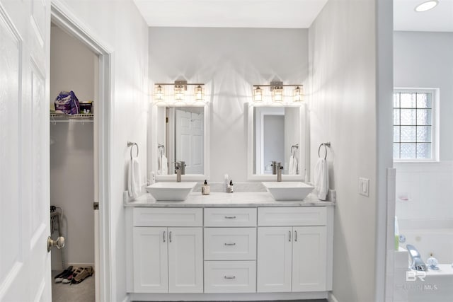 bathroom with double vanity, a tub with jets, and a sink