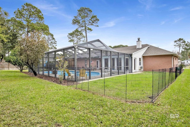 rear view of house with a lanai, fence, a lawn, a fenced in pool, and a chimney