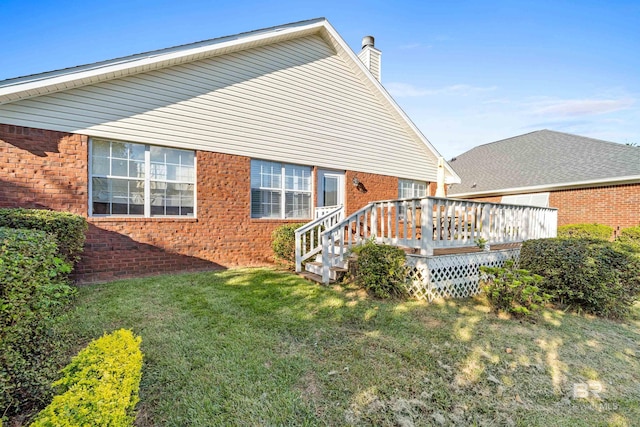 back of property with a chimney, brick siding, a yard, and a deck