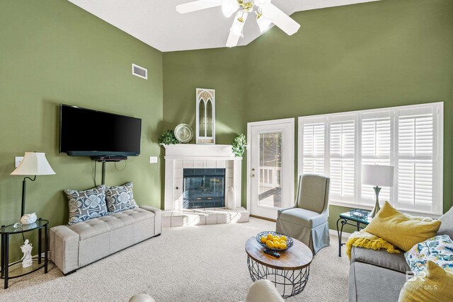 carpeted living area featuring visible vents, a ceiling fan, baseboards, a tiled fireplace, and high vaulted ceiling