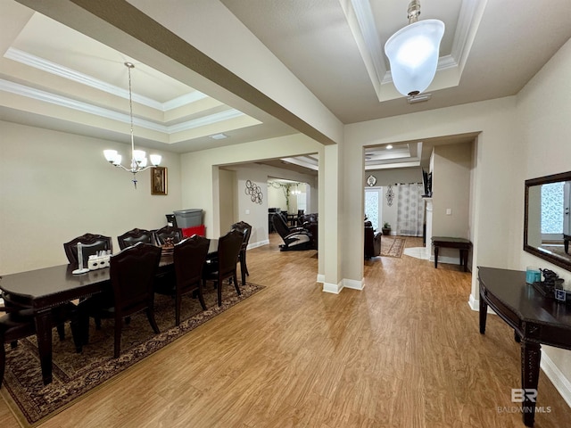 dining space featuring light hardwood / wood-style flooring, a healthy amount of sunlight, crown molding, a notable chandelier, and a raised ceiling