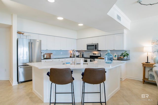 kitchen featuring appliances with stainless steel finishes, a center island with sink, decorative backsplash, and a kitchen breakfast bar