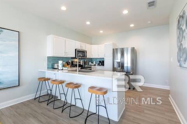 1492 Shell Ln, Gulf Shores, AL 36542 - kitchen with stainless steel appliances, a peninsula, a breakfast bar area, light wood-type flooring, and white cabinetry