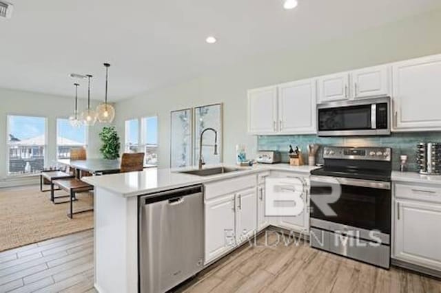 1492 Shell Ln, Gulf Shores, AL 36542 - kitchen with appliances with stainless steel finishes, a peninsula, light wood-style floors, tasteful backsplash, and white cabinets