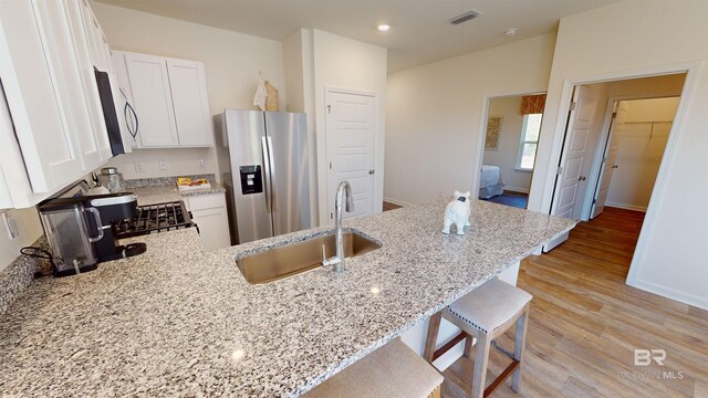 kitchen with a kitchen bar, stainless steel refrigerator with ice dispenser, white cabinetry, and light stone countertops