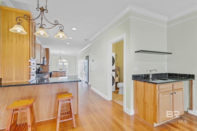 1328 W Lagoon Ave, Gulf Shores, AL 36542 - kitchen featuring stacked washer / dryer, freestanding refrigerator, light wood finished floors, dark stone countertops, and ornamental molding