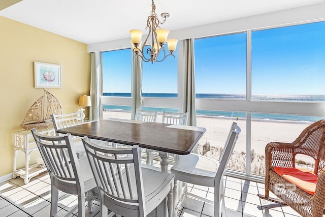 dining room featuring a view of the beach, a water view, an inviting chandelier, light tile patterned flooring, and baseboards