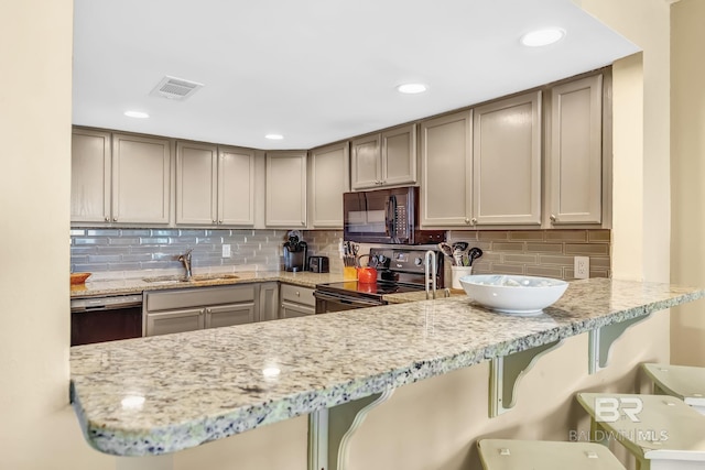 kitchen with black appliances, a sink, visible vents, and a kitchen breakfast bar