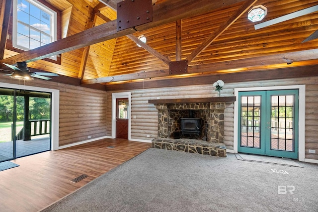 unfurnished living room with a towering ceiling, log walls, a wood stove, and a wealth of natural light