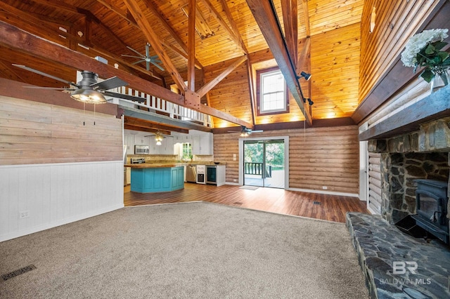 unfurnished living room featuring a wood stove, dark colored carpet, ceiling fan, wood ceiling, and beam ceiling