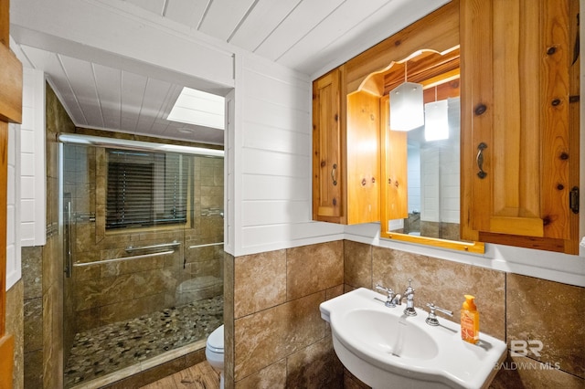 bathroom with an enclosed shower, sink, tile walls, and toilet