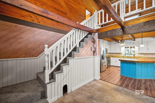 staircase featuring beam ceiling, hardwood / wood-style floors, ceiling fan, and wood walls