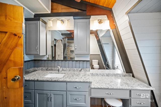 bathroom with vaulted ceiling, toilet, sink, and wood walls