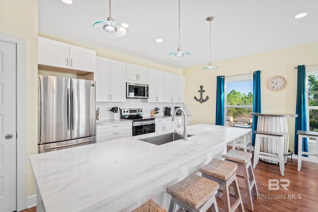 kitchen featuring dark wood-style flooring, stainless steel appliances, a kitchen bar, white cabinetry, and a sink