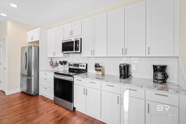 kitchen featuring light stone counters, stainless steel appliances, decorative backsplash, white cabinets, and light wood-type flooring