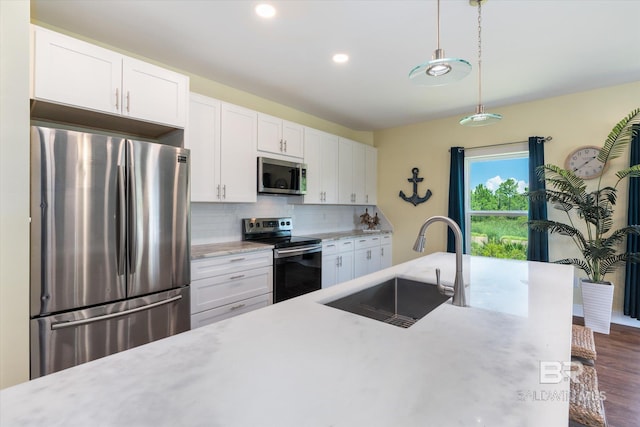 kitchen with appliances with stainless steel finishes, hanging light fixtures, a sink, white cabinetry, and backsplash