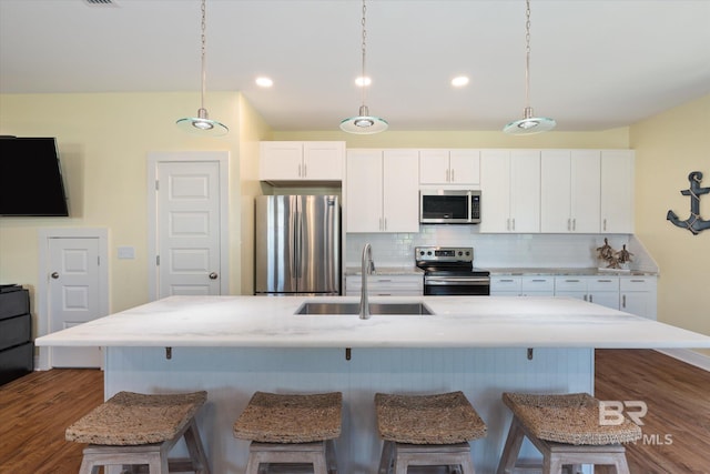 kitchen featuring tasteful backsplash, appliances with stainless steel finishes, white cabinets, a sink, and a kitchen bar