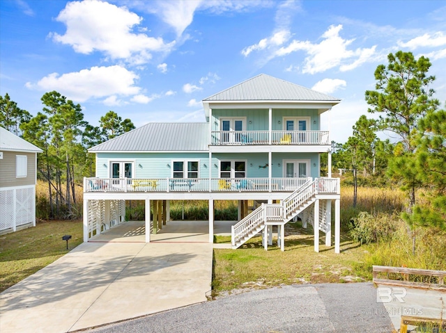 coastal inspired home with driveway, a balcony, stairway, and french doors