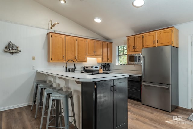 kitchen featuring stainless steel appliances, a peninsula, a breakfast bar area, light countertops, and vaulted ceiling