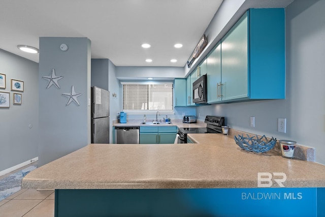 kitchen with a peninsula, blue cabinets, light countertops, stainless steel appliances, and a sink
