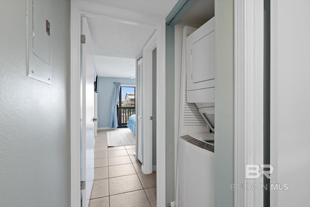 hall with light tile patterned floors, baseboards, and stacked washer and clothes dryer