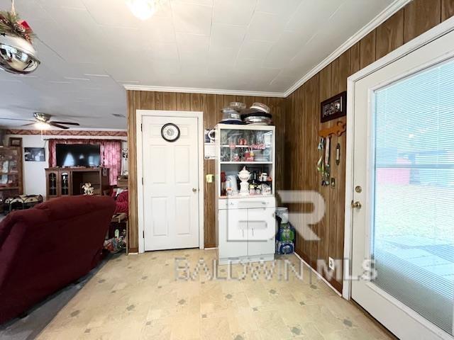 interior space featuring ceiling fan, wood walls, and crown molding